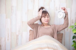 女性がベットの上で眠たい表情をしている